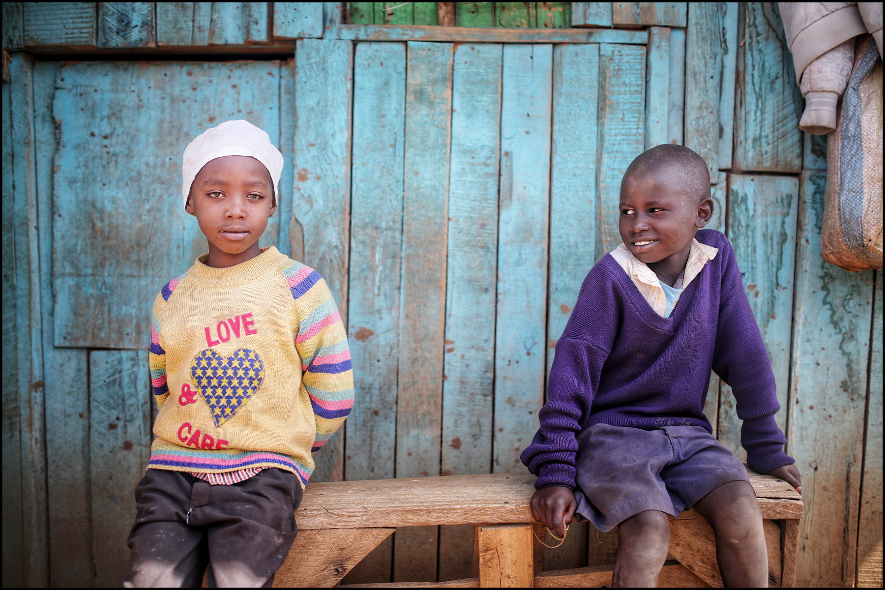 A travel storytelling slideshow featuring Murugi's photography: 2 of 9 - Two children sit on a bench in Kenya.